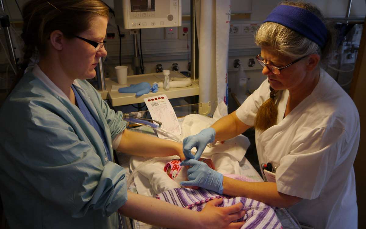 Lisbeth Hakvåg Nordseth og en av sykepleierne på nyfødtintensiv samarbeider om å få tatt blodprøven av Hanna. Foto: Grete Hansen.